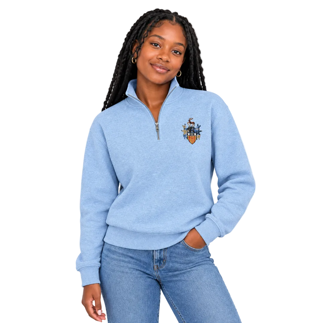 A woman modeling a light blue heathered quarter-zip sweatshirt with the University of Surrey crest embroidered on the left chest, paired with blue jeans against a plain white background.